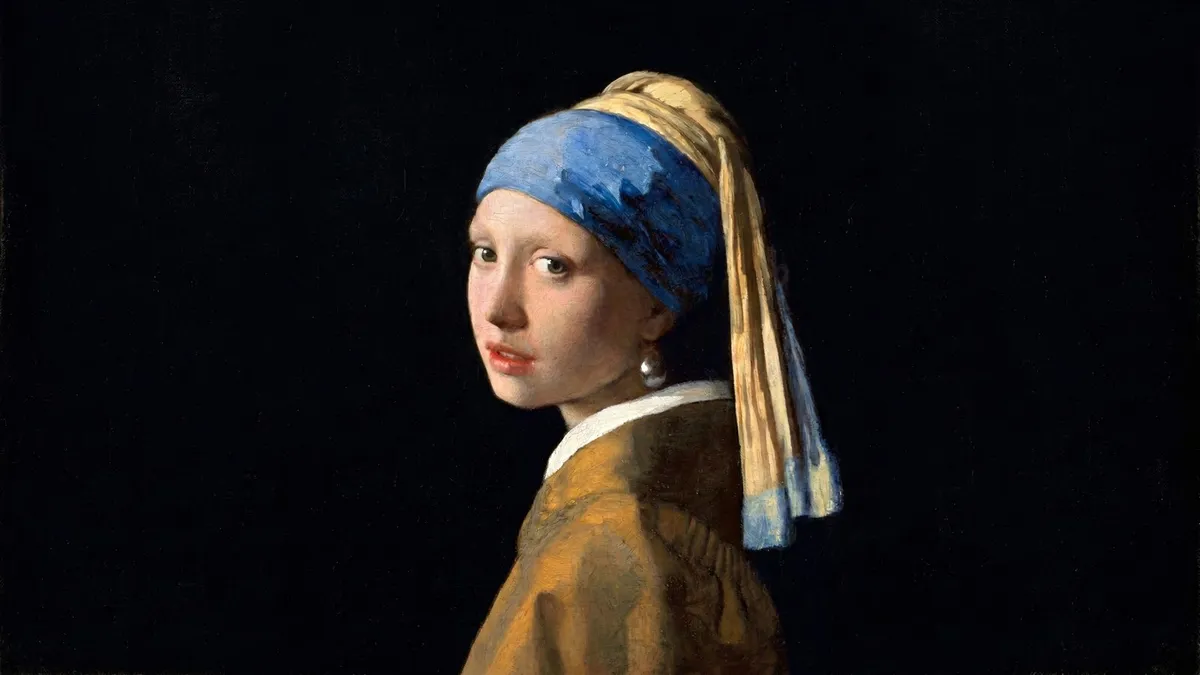 Young woman in a blue and yellow turban looking over her shoulder, wearing a pearl earring, against a black background