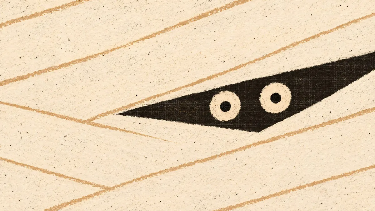 Close crop of a mummy's face made of wide cream bandage strips, with two round eyes peeking through a dark gap